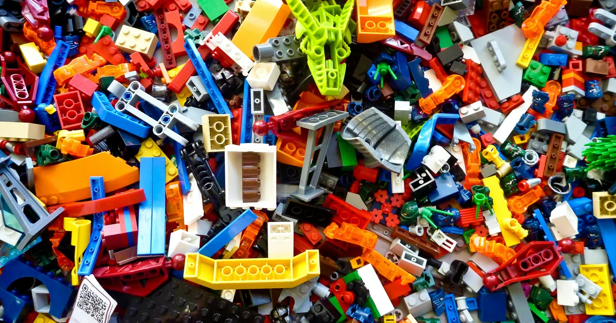 A dense pile of loose LEGO bricks in many colours, mixing plates, slopes, Technic beams and small printed parts with no box or instructions in sight