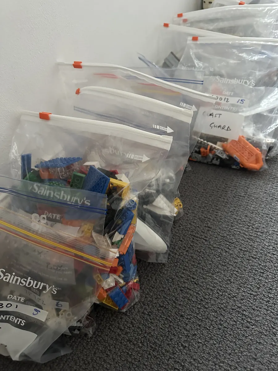 A row of labelled food bags, one per LEGO set, lined up against a wall.